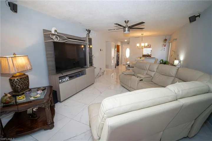 Living area with light marble finish flooring, a chandelier, a ceiling fan, and a textured ceiling