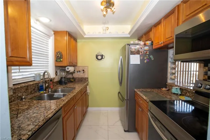 Kitchen with stainless steel appliances, brown cabinets, light marble finish flooring, dark stone countertops, and backsplash