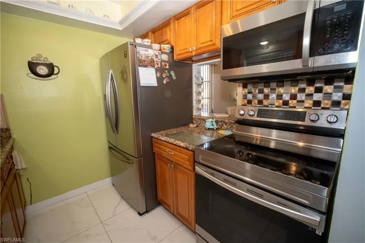 Kitchen featuring appliances with stainless steel finishes, brown cabinets, light marble finish floors, and decorative backsplash
