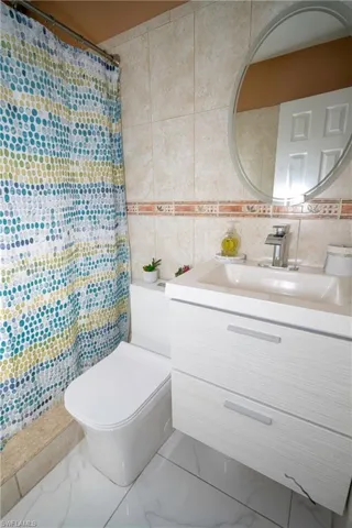 Bathroom with tile walls, vanity, marble finish floors, and decorative backsplash