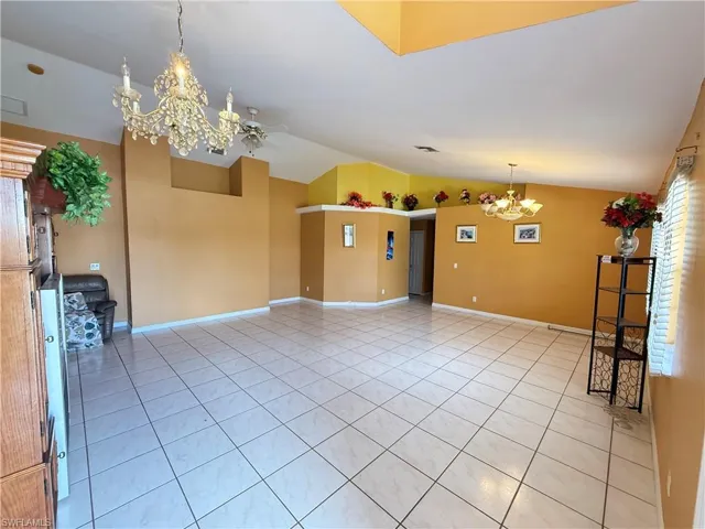 Empty room with a chandelier, light tile patterned floors, and lofted ceiling