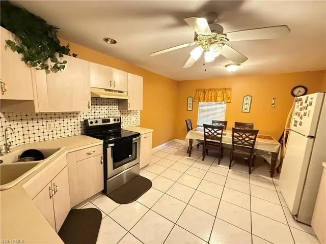Kitchen featuring electric range, light countertops, freestanding refrigerator, a ceiling fan, and light tile patterned floors