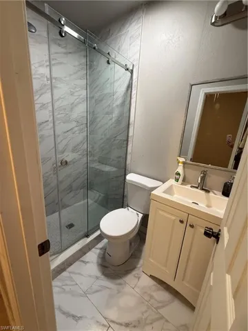 efficiency bathroom bathroom featuring vanity, a stall shower, light marble finish floors, and a textured wall