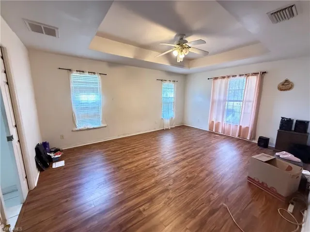 Unfurnished living room featuring a raised ceiling, ceiling fan, and dark wood-style floors