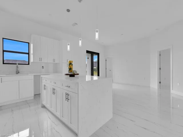 Kitchen featuring a center island, white cabinets, sink, light tile floors, and pendant lighting