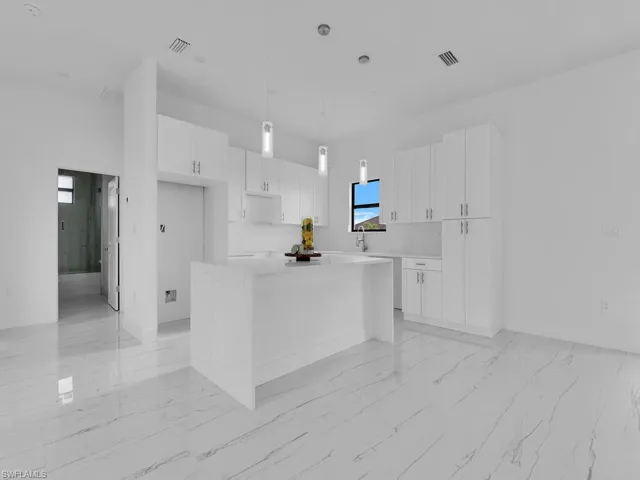 Kitchen featuring decorative light fixtures, white cabinets, light tile floors, and a kitchen island