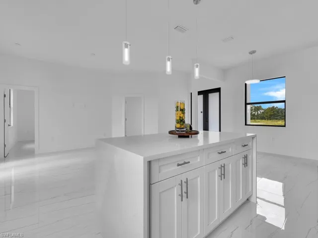 Kitchen with hanging light fixtures, white cabinetry, light tile floors, and a kitchen island