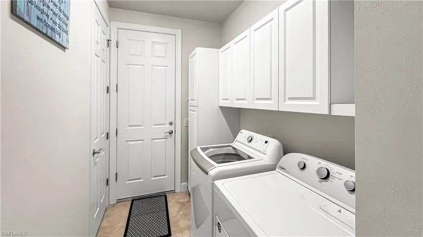 Clothes washing area featuring cabinets, washing machine and dryer, and light tile patterned flooring