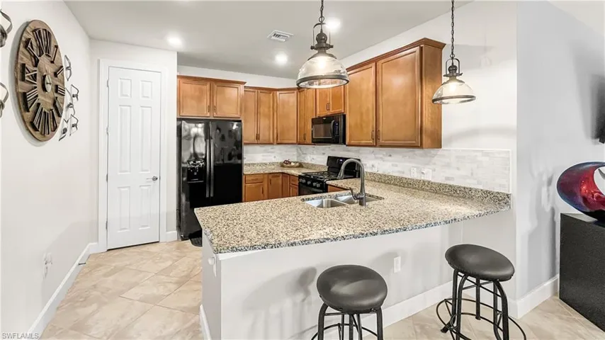 Kitchen featuring a kitchen breakfast bar, hanging light fixtures, sink, and black appliances