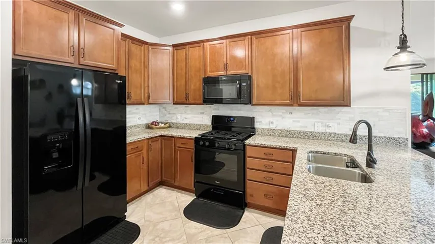 Kitchen with hanging light fixtures, black appliances, sink, and light stone countertops