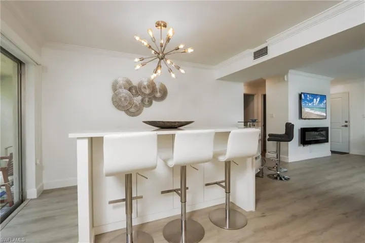 Kitchen featuring crown molding, light wood-style flooring, a kitchen breakfast bar, a chandelier, and a glass covered fireplace