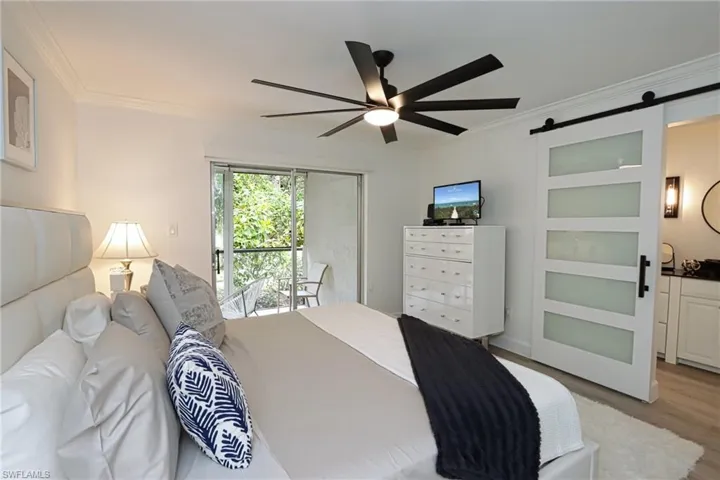 Bedroom featuring ornamental molding, a barn door, light wood finished floors, access to outside, and ceiling fan