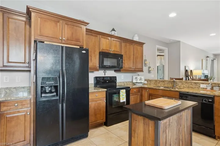 Kitchen featuring black appliances, dark stone countertops, light tile patterned floors, and sink