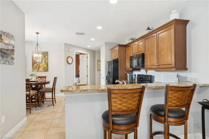 Kitchen with light stone counters, kitchen peninsula, pendant lighting, light tile patterned flooring, and black appliances