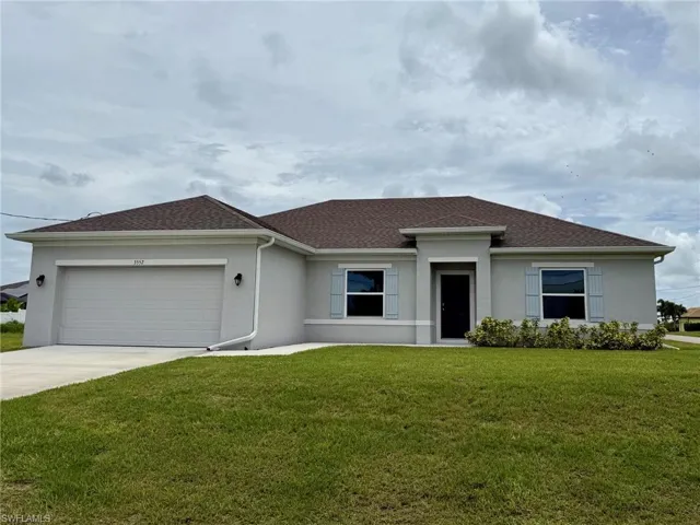 View of front of home with stucco siding, concrete driveway, a front lawn, and an attached garage