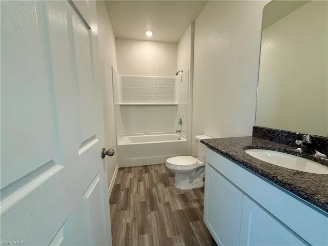 Bathroom with bathing tub / shower combination, vanity, dark wood-type flooring, and a textured wall