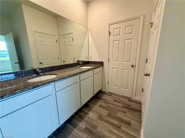 Bathroom featuring double vanity, dark wood-style floors, and a textured wall