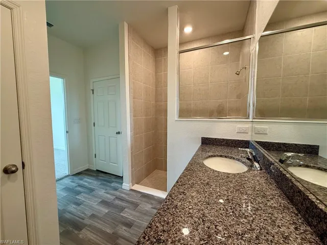 Bathroom featuring a stall shower, double vanity, and dark wood finished floors