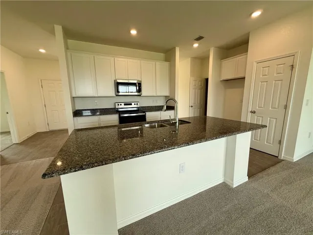 Kitchen featuring dark colored carpet, white cabinets, recessed lighting, dark stone counters, and appliances with stainless steel finishes