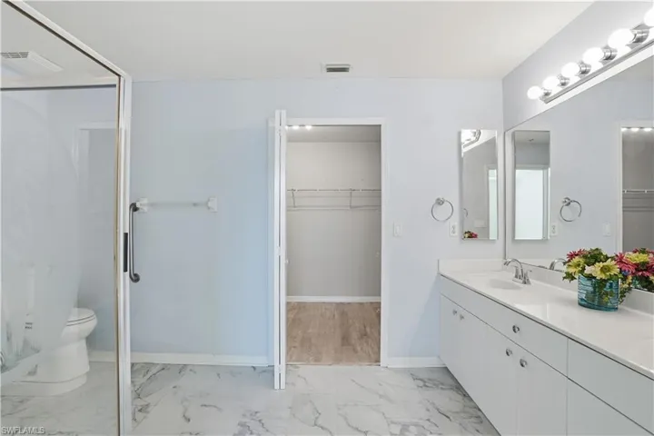Bathroom featuring light marble finish floors, a spacious closet, vanity, and a stall shower