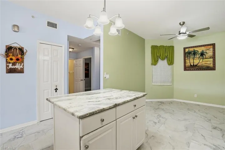 Kitchen with white cabinets, decorative light fixtures, light marble finish flooring, a chandelier, and a center island