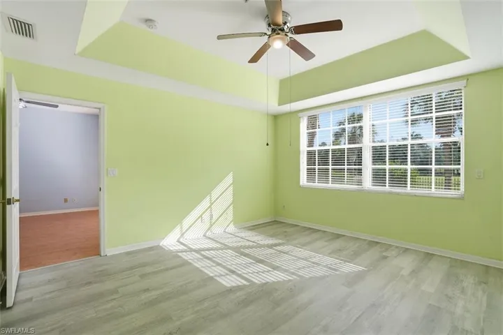 Unfurnished room featuring a raised ceiling, ceiling fan, and light wood finished floors