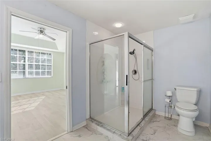 Bathroom featuring a shower stall, ceiling fan, and light marble finish floors