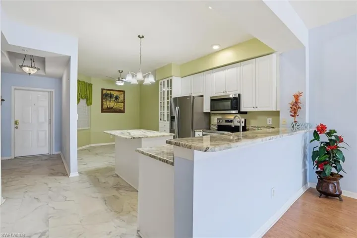 Kitchen with white cabinets, light stone counters, appliances with stainless steel finishes, decorative light fixtures, and a kitchen island
