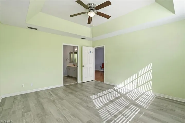 Unfurnished bedroom featuring a raised ceiling, wood finished floors, a ceiling fan, and ensuite bath