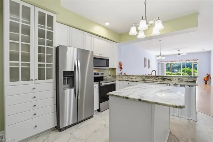 Kitchen with appliances with stainless steel finishes, glass insert cabinets, white cabinetry, hanging light fixtures, and recessed lighting