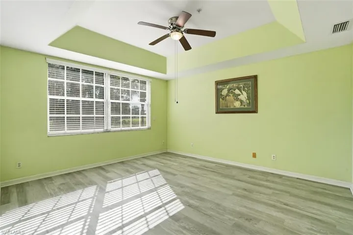 Empty room with a tray ceiling, light wood finished floors, and ceiling fan