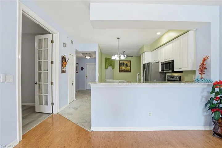 Kitchen featuring light wood finished floors, white cabinets, light stone counters, hanging light fixtures, and stainless steel appliances
