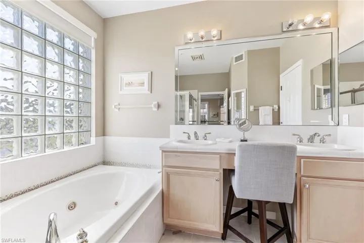 Full bath featuring a healthy amount of sunlight, double vanity, a jetted tub, and a sink