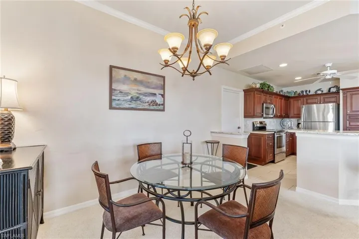 Dining area featuring ceiling fan with notable chandelier, crown molding, light carpet, and baseboards