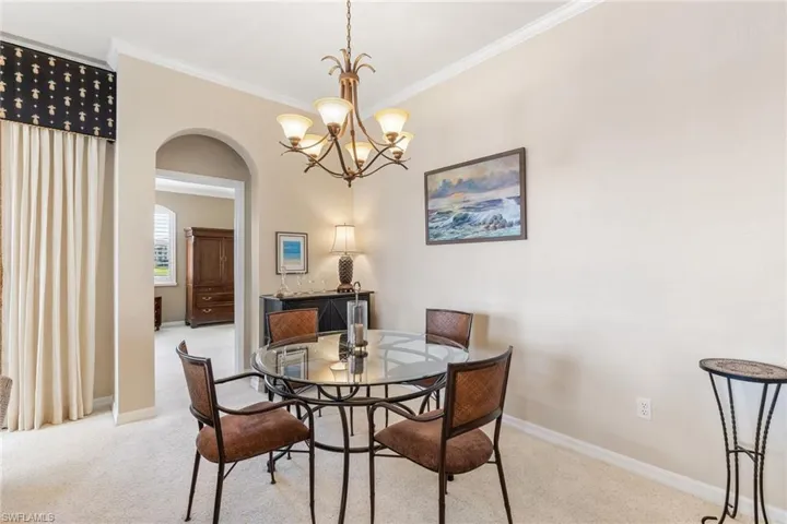 Carpeted dining area featuring an inviting chandelier, baseboards, arched walkways, and crown molding