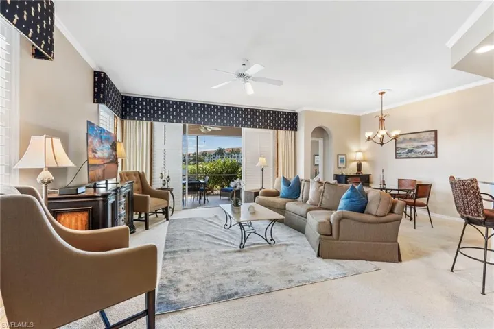 Living room featuring carpet, arched walkways, crown molding, baseboards, and ceiling fan with notable chandelier