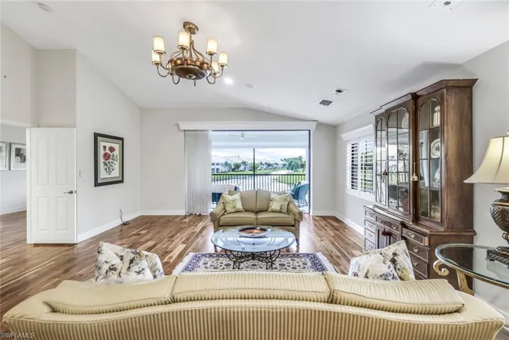 Living room with Acacia wood floors, a chandelier, and vaulted ceiling