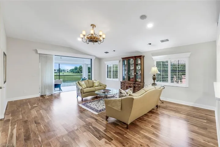 Living room with Acacia wood floors, a chandelier, and vaulted ceiling