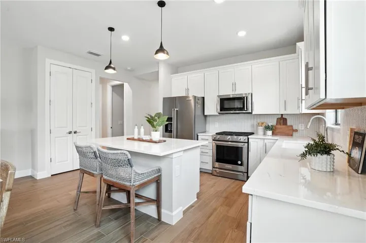 Kitchen with high end appliances, white cabinetry, decorative backsplash, light wood finished floors, and recessed lighting