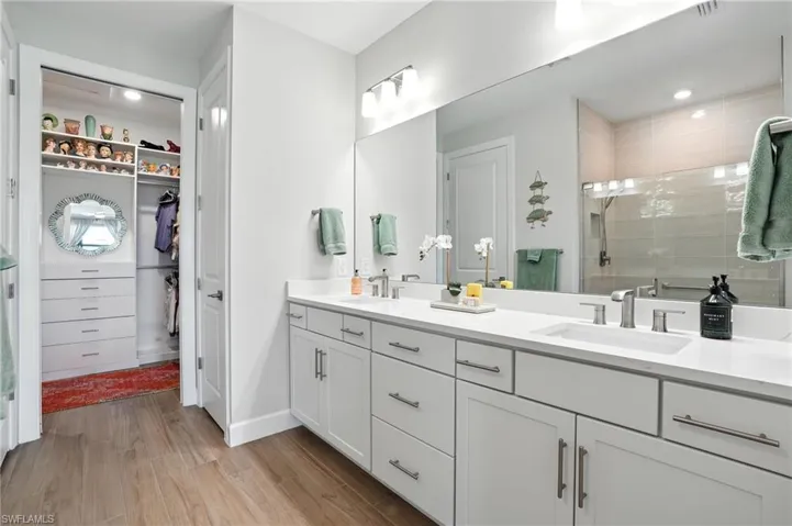Full bath featuring double vanity, a stall shower, wood finished floors, and a spacious closet
