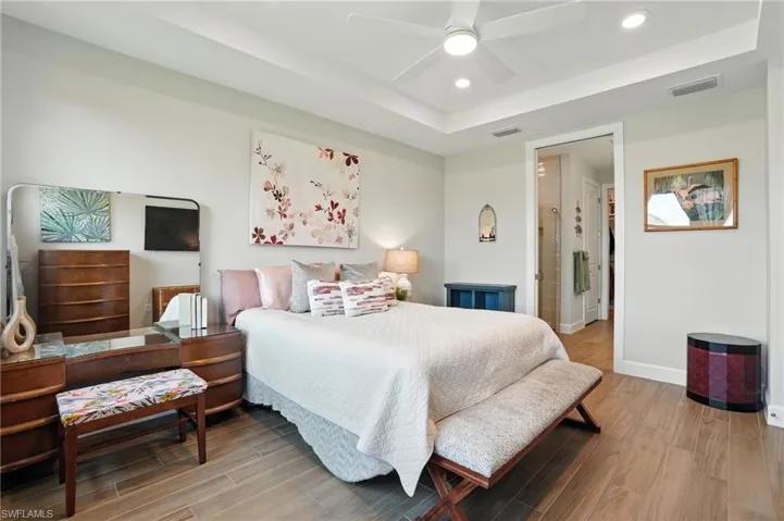 Bedroom featuring light wood finished floors, a raised ceiling, recessed lighting, and ceiling fan
