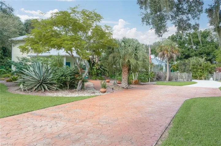 Front of home with wide stamped concrete driveway and walkway.  Lots of beautiful landscaping with mature trees.