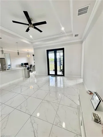 Spare room featuring french doors, a tray ceiling, crown molding, light marble finish flooring, and a ceiling fan