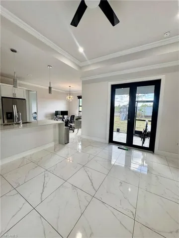 Unfurnished living room featuring french doors, a chandelier, crown molding, light marble finish flooring, and a tray ceiling