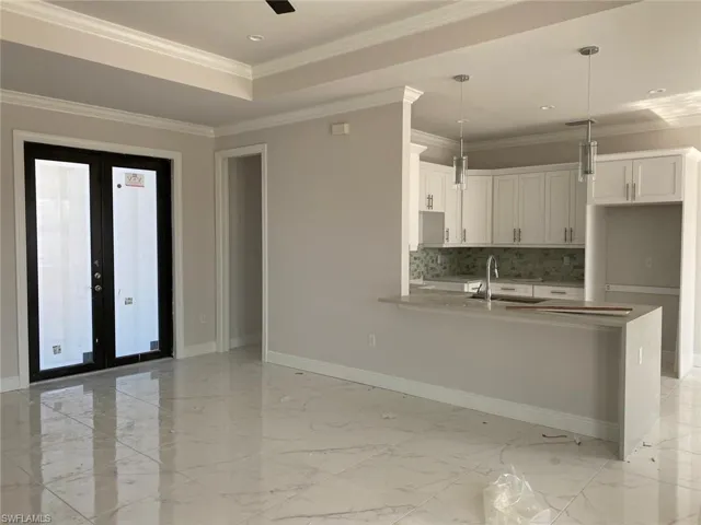 Kitchen with white cabinetry, pendant lighting, light marble finish floors, a peninsula, and ornamental molding