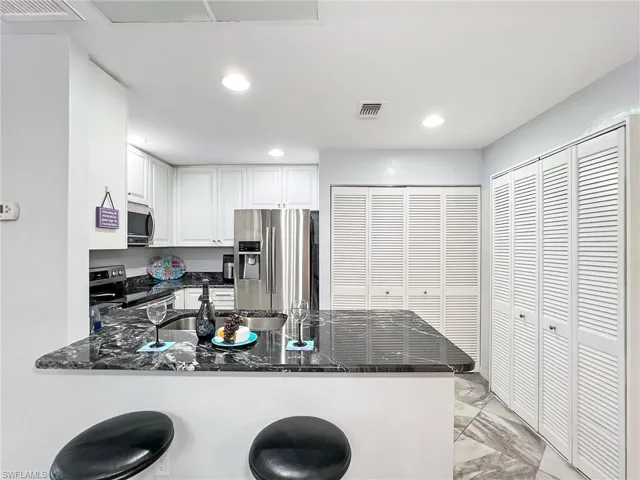 Kitchen with appliances with stainless steel finishes, white cabinets, a kitchen bar, kitchen peninsula, and dark stone counters