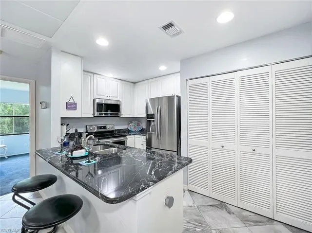 Kitchen with kitchen peninsula, stainless steel appliances, dark stone counters, and a breakfast bar