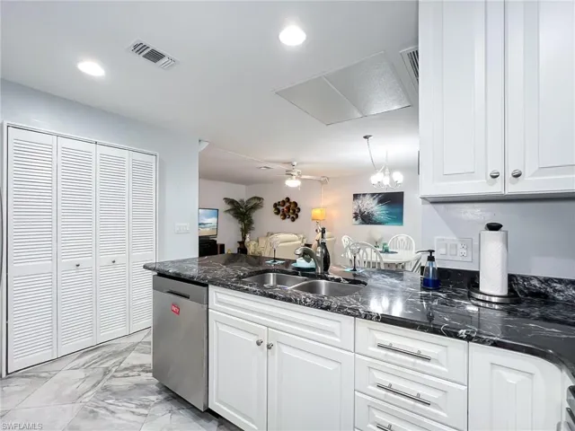Kitchen featuring dark stone countertops, ceiling fan with notable chandelier, white cabinetry, sink, and stainless steel dishwasher