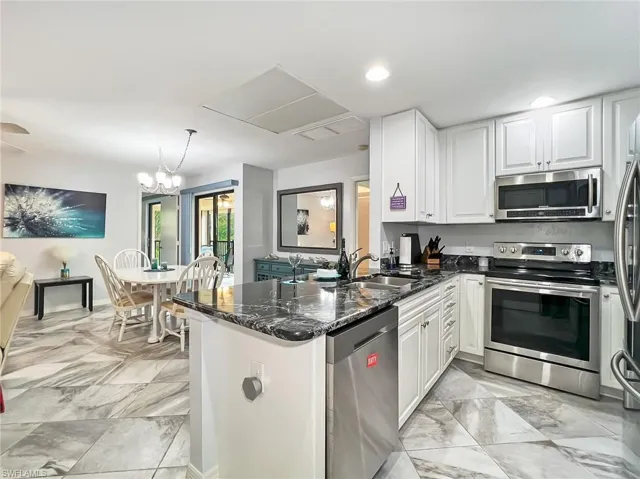 Kitchen featuring dark stone countertops, white cabinetry, kitchen peninsula, sink, and appliances with stainless steel finishes
