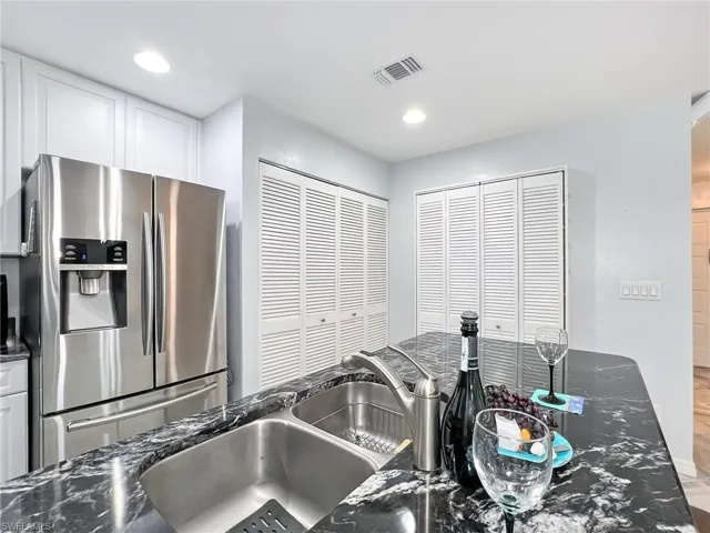 Kitchen featuring hardwood / wood-style flooring, dark stone counters, stainless steel fridge with ice dispenser, and white cabinets